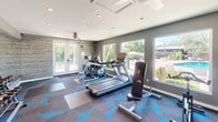 Located in Carrboro, NC, this fitness center is a thoughtfully designed exercise space that maximizes functionality within its compact footprint. The room features a modern aesthetic, highlighted by striking geometric-patterned carpet in shades of gray and blue that adds a dynamic visual energy to the space.

The facility is well-stocked with a comprehensive range of equipment to support diverse workout routines. Cardio options include a treadmill and an elliptical trainer, while strength training is served by a multi-function cable machine, a weight bench, and a tiered dumbbell rack with a full set of free weights. A ceiling fan with recessed lighting overhead ensures a comfortable environment during workouts.

One of the standout features of this space is its abundant natural light, courtesy of large picture windows and a set of French doors that open to an outdoor area. These windows frame views of lush greenery and what appears to be a pool area, creating an airy, connected-to-nature atmosphere. A textured wood-panel accent wall adds warmth and visual interest, contrasting pleasingly with the cool gray walls. Full-length mirrors are strategically placed to enhance the sense of space and assist with form during exercise, making this fitness center both practical and inviting.