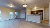 This single-floor unit at 18906 8th Avenue NW offers a thoughtfully arranged layout with a clean, contemporary aesthetic throughout. The open-concept living and dining area is finished with light hardwood-style flooring and benefits from natural light streaming through a glass door that opens to a balcony with tree-lined views. Pendant and flush-mount lighting fixtures illuminate the space, complementing the warm, neutral wall tones found throughout the unit.

The kitchen is defined by a peninsula counter that separates it from the living area, providing both workspace and a casual dining option. Rich, dark-toned cabinetry pairs with white countertops and a full suite of stainless steel appliances, including a refrigerator, range, and microwave. A dedicated laundry area houses a full-sized top-load washer and dryer with overhead wire shelving for added storage convenience.

A central hallway connects the living spaces to multiple carpeted bedrooms, each featuring windows with outdoor views of surrounding trees and neighboring structures. The bathroom is well-appointed with a dark wood vanity, white countertop, a large mirror, and a full-sized soaking tub with a clean white surround. Light hardwood-style flooring extends through the bathroom, maintaining consistency with the rest of the unit.