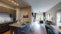 This thoughtfully designed single-floor residence offers a seamless open-concept layout connecting the kitchen, dining, and living areas. The kitchen is outfitted with dark wood cabinetry, granite countertops, a subway tile backsplash, track lighting, and a central island with bar seating — ideal for casual dining and entertaining. The adjoining dining area flows naturally into the expansive living room, which features wood-look flooring, a ceiling fan, and a large sliding glass door that fills the space with natural light and provides direct outdoor access.

The primary bedroom continues the floor-to-ceiling window theme, offering generous natural light, plush carpet flooring, and a serene ambiance. A second bedroom is equally well-appointed, featuring carpet, a walk-in closet, and neutral tones. The bathroom includes granite-topped dark wood vanity cabinetry, wood-look flooring, and a walk-in shower.

Throughout the residence, warm neutral wall tones, recessed lighting, and arched architectural details contribute to a cohesive and polished aesthetic. The consistent use of granite surfaces and rich cabinetry ties each room together, while the abundance of natural light and outdoor views enhance the overall sense of openness and comfort.