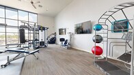 Located at 4333 N 6th Dr in Phoenix, AZ, this fitness center offers a thoughtfully designed workout space with impressive architectural details and a full complement of exercise equipment. The single-floor facility is characterized by soaring ceilings that create an open, airy atmosphere, while expansive floor-to-ceiling windows along one wall flood the space with abundant natural light and provide views of the surrounding neighborhood.

The interior features neutral-toned carpet flooring throughout and clean white walls that contribute to a bright, modern aesthetic. A ceiling fan provides additional air circulation, complementing the overall comfort of the space.

The fitness area is comprehensively equipped to support a wide variety of workout routines. Strength training options include a Synrgy360 functional training rig, a cable machine, a Smith machine with free weights, and an adjustable weight bench. A dedicated dumbbell rack and weight plates are also available. For flexibility and functional fitness, a tiered rack holds multiple stability and medicine balls in assorted sizes. Cardio equipment, including a step machine, rounds out the offerings. Wall-mounted flat-screen televisions are positioned throughout the space for entertainment during workouts. Full-length mirrors on one wall allow users to monitor their form, enhancing the overall training experience.