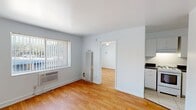 This efficiently designed 430-square-foot, one-bedroom, one-bathroom apartment offers a functional single-floor layout. The galley-style kitchen features white cabinetry, dark countertops, a double stainless steel sink, and tile flooring, with ample upper and lower cabinet storage. A full-size white refrigerator and a gas range complete the kitchen's practical setup. The 130-square-foot bedroom is bright and airy, showcasing warm hardwood flooring, a ceiling fan with integrated lighting, wall sconces, and a large window with vertical blinds that allow natural light and outdoor views. A louvered closet door provides storage, and a wall-mounted HVAC unit ensures year-round climate control. The bathroom is finished with light tile flooring, warm earth-toned stone tile accents surrounding the shower, a pedestal sink, a wall-mounted storage cabinet, and a mirrored medicine cabinet. The unit's clean white walls and neutral palette throughout create a bright, cohesive ambiance. The overall layout, as seen in the dollhouse view, is compact yet well-organized, making efficient use of every square foot across the kitchen, bedroom, and bathroom.