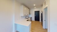 Located on Washburn Ave S in Minneapolis, Minnesota, this single-floor unit showcases a thoughtfully designed interior with modern finishes throughout. The kitchen is a standout feature, outfitted with crisp white shaker-style cabinetry accented by matte black hardware, a herringbone tile backsplash, white quartz countertops, and a suite of stainless steel appliances including a dishwasher and range with a wall-mounted hood vent. A double-basin sink with a matte black faucet adds a refined touch, while a peninsula provides additional prep and dining space. Light wood-tone flooring runs throughout the unit, lending warmth and continuity to the open layout. The living area benefits from a row of tall vertical windows that invite natural light and offer views of the surrounding neighborhood, complemented by a modern ceiling fan with integrated lighting. The bathroom is clean and functional, featuring a full tub-shower combination with white tile surround, chrome fixtures, and matte black accent hardware. The overall color palette — crisp whites, soft neutrals, and black accents — creates a cohesive, contemporary aesthetic. The unit's efficient single-floor layout ensures easy navigation between living, cooking, and private spaces.