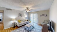 This single-floor residence offers a thoughtfully organized layout across several distinct living areas. The living room serves as the central gathering space, featuring wood-look flooring, a ceiling fan with light fixture, and a textured ceiling. A sliding glass door with vertical blinds fills the room with natural light while providing outdoor access. The neutral gray walls and open layout lend the space a clean, welcoming ambiance.

Adjacent to the living room, the dining area is defined by a pendant chandelier overhead and chair-rail molding along the walls, creating a subtle architectural detail. It connects directly to the galley-style kitchen, which is equipped with warm wood cabinetry, granite-look countertops, black appliances including a refrigerator and range, and a stainless steel sink. Ample upper and lower cabinet storage lines both walls of the kitchen.

The residence includes two bedrooms, each carpeted and featuring a ceiling fan with lighting. Both rooms offer a quiet, restful atmosphere with generous wall space and natural light from windows. The full bathroom includes a wood vanity with a granite-look countertop, a single sink, and a shower-tub combination with a decorative curtain, complemented by wood-look flooring throughout.