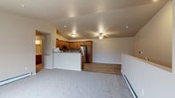 This single-floor unit offers a well-designed open-concept layout that seamlessly connects the kitchen and living areas. The kitchen is equipped with warm-toned wood cabinetry, granite-style countertops, and a full suite of stainless steel appliances, including a refrigerator, electric range, over-the-range microwave, and dishwasher. A peninsula counter separates the kitchen from the adjoining space, providing additional prep and serving area. The living area features durable wood-style flooring that transitions into plush carpeting, with a ceiling fan overhead and baseboard heating along the walls. Sliding glass doors lead to a private balcony, allowing natural light to fill the space. The bedrooms are generously sized, each with soft carpeting, ceiling fans, individual windows, and baseboard heating; at least one bedroom includes a closet with sliding doors. The bathroom features wood-style flooring, a granite-style vanity countertop with an undermount sink, warm wood cabinetry with open shelving, a walk-in shower, and a large mirror with overhead lighting. The unit's neutral color palette and consistent finishes throughout create a cohesive, functional living environment.