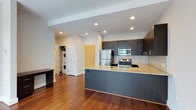This single-floor residence showcases a thoughtfully designed open-concept layout with rich hardwood flooring flowing throughout the main living areas. The kitchen serves as a central focal point, featuring dark espresso cabinetry extending to the ceiling, light granite countertops, and a white square-tile backsplash. A peninsula with matching granite provides additional workspace and a natural division between the kitchen and living area. Stainless steel appliances, including a refrigerator, range, and built-in microwave, complete the well-equipped kitchen.

The open living area offers a clean, versatile space bathed in natural light from large floor-to-ceiling windows that frame urban views of the surrounding cityscape. A dedicated bedroom, finished with neutral carpet, also benefits from generous window exposure and natural light.

The bathroom features a full tub-shower combination with large-format warm-toned wall tiles, built-in corner shelving, and a granite-topped vanity with chrome fixtures. A practical in-unit laundry area with a stacked washer and dryer is conveniently accessible off the main living space. Recessed lighting throughout adds a polished, modern ambiance to the entire unit.