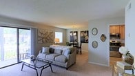 Located at 3104 Turtle Point Dr in Fayetteville, North Carolina, this single-floor home offers a comfortable and well-appointed living environment with a thoughtfully designed open floor plan. The living area serves as the heart of the home, featuring plush carpeting, neutral-toned walls, and an abundance of natural light streaming through large windows dressed with blinds. A stylish sofa anchors the space, complemented by a glass-top coffee table and carefully selected wall art that adds a contemporary touch to the room's warm ambiance. The living area flows seamlessly into the dining space, which is highlighted by an elegant pendant chandelier that casts a warm glow over the dining table and chairs. Decorative oval mirrors adorn the adjacent wall, adding depth and visual interest to the transition between spaces. The overall aesthetic throughout is modern and cohesive, with a neutral color palette of soft grays and warm whites that creates a calm, inviting atmosphere. The single-level layout ensures easy accessibility and a natural sense of flow from room to room. This home combines functional design with stylish finishes, making it a comfortable and visually appealing residence in the Fayetteville area.
