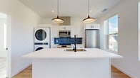 Located at 2017 West 44th Street in Cleveland, Ohio, this thoughtfully designed one-bedroom, one-bathroom unit offers a modern, efficient layout on a single floor. The open-concept living and kitchen area is bright and airy, with light hardwood flooring, recessed lighting, and large windows that flood the space with natural light and provide views of the surrounding neighborhood.

The kitchen is a standout feature, centered around a white waterfall island with an undermount sink and matte black faucet. White shaker cabinetry, a bold navy blue tile backsplash, stainless steel appliances — including a full-size refrigerator, range, and microwave — and stylish pendant lighting complete the space. A stacked washer and dryer unit is conveniently integrated into the kitchen area.

The bedroom is carpeted for comfort, featuring a closet and a large window that brings in ample natural light. The bathroom includes a white vanity with black hardware, tile flooring in a slate-gray tone, and a tub-shower combination with white subway tile surround and matte black fixtures.

Clean white walls, consistent black hardware accents throughout, and contemporary finishes give this unit a cohesive, modern aesthetic.
