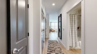 This single-floor, 2-bedroom, 2-bathroom residence offers a well-designed layout with modern finishes and a clean, contemporary aesthetic throughout. The open-concept kitchen and living area serves as the heart of the home, featuring a striking white kitchen with sleek cabinetry, a decorative tile backsplash, stainless steel appliances, and a large island with seating — ideal for both casual dining and entertaining. Light wood-tone flooring flows seamlessly through the main living areas, complementing the bright, white walls. The living room benefits from a generous bank of windows that flood the space with natural light and provide outdoor views. A well-appointed hallway connects the main living area to the private quarters, featuring stylish gray panel doors and recessed lighting. The primary bedroom is a comfortable retreat with plush carpeting, a ceiling fan, and a window with outdoor views. It is accompanied by a spacious walk-in closet outfitted with extensive shelving and hanging rod systems. The second bedroom is equally inviting, with natural light filtering through large windows. Both bathrooms are finished with wood-look flooring, clean white vanities, and shower-tub combinations. The overall ambiance is modern, bright, and move-in ready.