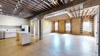 Located on S Buck St in Cincinnati, OH, this industrial-style loft offers a distinctive blend of raw architectural character and modern functionality across a single, generously sized floor. Exposed brick walls, open wood-beam ceilings, and polished concrete floors define the aesthetic throughout, creating a warehouse-inspired ambiance that is both spacious and visually striking.

The main living areas feature expansive open floor plans bathed in natural light from multiple windows dressed with patterned curtains. The kitchen is well-appointed with light maple cabinetry, stainless steel appliances including a gas range, microwave, and French door refrigerator, a central island, and a deep farmhouse-style double sink with a stainless steel backsplash.

The primary bedroom is notably generous in size, featuring exposed beam ceilings and open-style closet storage with curtained partitions. The second bedroom echoes the same industrial character. Both bathrooms are functional, with one featuring a full tub-shower combo. A dedicated laundry room includes a full-size washer and dryer alongside an electrical panel. A hallway and closet complete the layout, offering practical storage solutions within this unique, character-rich Cincinnati loft.