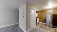 Located at 6615–6635 Charles St in Philadelphia, PA, this single-floor unit offers a practical and efficiently laid-out living space. The living room is a comfortable, open area finished with soft gray carpeting and crisp white walls, with a baseboard heating system running along the perimeter. A window allows natural light to brighten the room, creating an airy feel despite the compact footprint. The transition from the living room leads to the kitchen area, which features warm wood-paneled walls that add a classic character to the space. The kitchen is equipped with white cabinetry, a stainless steel refrigerator, and a range, all set atop light wood-look flooring that contrasts neatly with the carpeted living area. Two closets provide practical storage solutions within the unit. The bathroom includes a full tub and shower combination with white surround walls and chrome fixtures, maintaining a clean and functional aesthetic. Overall, the unit presents a straightforward, no-frills interior with a mix of classic finishes including wood paneling and neutral tones, making it a practical option in the northeast Philadelphia neighborhood of Mayfair.