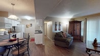 Located at 11444 Vance Jackson Rd in San Antonio, Texas, this single-floor unit offers a well-organized and functional layout. The living room is warm and inviting, featuring rich hardwood-style flooring, a textured ceiling, and large sliding glass doors dressed with vertical blinds and sheer curtains that allow abundant natural light to fill the space. The open-concept design connects the living area to the kitchen, which is equipped with white cabinetry, dark countertops, and full-size appliances including a refrigerator and range. A pass-through counter provides a natural transition to the dining area, which features a pendant light overhead and a window that brings in additional daylight. The bedroom offers plush carpeting, a ceiling fan, and a generously sized window with layered sheer curtains, creating a restful retreat. A closet provides practical storage. The bathrooms are neatly appointed with dark countertops, white cabinetry, and tile flooring. One bathroom connects directly to the bedroom, offering added privacy and convenience. Throughout the unit, neutral wall tones and consistent flooring create a cohesive and comfortable atmosphere, making this a practical and livable space in a convenient San Antonio location.