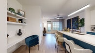 Located in Charlotte's vibrant South End neighborhood, this single-floor residence at 1115 S Mint St offers a well-appointed layout with thoughtfully designed interiors throughout. The kitchen serves as a striking focal point, showcasing two-tone cabinetry with deep teal lower cabinets, crisp white uppers, and gold hardware accents. Stainless steel appliances, a white quartz countertop, and a matching island with bar seating complete the space, combining functionality with bold visual appeal. Light wood-style flooring flows through the open-concept living and dining areas, where large windows and a glass balcony door invite abundant natural light and outdoor views. The living area provides a welcoming retreat with generous wall space and direct balcony access. The primary bedroom features plush carpeting, large windows with views, and an en-suite bathroom appointed with a dual-sink teal vanity, gold hardware, black matte fixtures, and a glass-enclosed walk-in shower with white tile surround. A spacious walk-in closet with wire shelving and a stacked in-unit washer and dryer adds practical convenience. A second bedroom offers the same clean, calm aesthetic with hardwood-style flooring and ample closet space. Integrated built-in shelving in the living area provides additional storage and display options throughout.