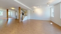 Located at 34 Main St in North Easton, Massachusetts, this multi-floor property showcases a thoughtful blend of contemporary updates and historic character. The main living level features a bright, open kitchen equipped with stainless steel appliances, white cabinetry, a subway tile backsplash, and light hardwood flooring, all bathed in natural light from large windows overlooking the outdoors. Original exposed timber beams appear throughout, adding warmth and architectural interest to the otherwise clean, modern aesthetic. Carpeted rooms across the floors offer comfortable, versatile spaces, including areas with angled, vaulted ceilings on the upper level that lend a distinctive character to the layout. Natural light is introduced through both standard windows and elevated clerestory-style windows in select rooms. The primary bathroom is well-appointed with a dual-sink vanity, generous mirror, accessibility grab bars, and a dedicated bathing area, while an additional full bathroom includes a tub/shower combination and tile flooring. A spacious walk-in closet with built-in wire shelving provides ample storage. A dedicated laundry area with an in-unit washer adds everyday convenience. Across all three floors, the space maintains a clean, neutral palette with white walls, light trim, and warm carpeting, creating a cohesive and welcoming environment throughout.