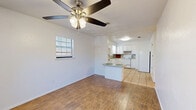 This well-organized 2-bedroom, 1-bathroom single-story residence offers a practical and comfortable layout across its single floor. The open-concept living, dining, and kitchen area serves as the heart of the home, featuring warm wood-look flooring, a ceiling fan with light fixture, and a window fitted with blinds that allows natural light to fill the space. A peninsula-style kitchen counter with granite-look surfaces provides additional prep and dining space, while the kitchen itself is appointed with white cabinetry, a white electric range, refrigerator, dishwasher, and a utility area housing a full-size washer and dryer. Light tile flooring extends throughout the kitchen and utility zones. Both bedrooms are carpeted and include ceiling fans, windows with blinds for natural light, and access to closets with built-in shelving. The primary bedroom offers a generous footprint with wainscoting-style wall trim detailing. The bathroom features a full soaking tub with a tiled surround in a neutral stone-look finish. Three closets throughout the unit provide notable storage capacity. The home's clean white walls, consistent finishes, and functional layout create a bright, easy-to-maintain living environment.