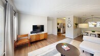 Located at 1100 Pulaski St in Columbia, SC, this one-bedroom, one-bathroom residence offers a thoughtfully designed single-floor layout. The living room is a standout space, featuring large windows that flood the room with natural light, wood-style flooring, crown molding, and a textured ceiling. A bold blue accent wall adds a distinctive design touch, complementing the open sightline to the kitchen, which is equipped with stainless steel appliances including a refrigerator, range, and microwave. The bedroom provides a comfortable retreat with plush carpet, a ceiling fan, natural light from windows, and a rich teal accent wall that creates a warm, grounded ambiance. The bathroom is well-appointed with a granite-topped vanity, white cabinetry with brushed nickel hardware, a large mirror, wood-style flooring, and a full shower-tub combo with a tile surround. Additional spaces include a dedicated entrance, a closet for storage, and a private in-unit laundry area equipped with a washer and dryer and wire shelving above. The overall design balances neutral tones with tasteful accent colors, creating a cohesive and functional living environment.