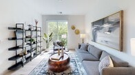 Located at 4407 E Main St in Richmond, Virginia, this single-floor unit showcases a contemporary design with a clean, neutral palette and light wood-style flooring throughout. The kitchen is outfitted with white shaker cabinetry extending to the ceiling, quartz countertops, a gray subway tile backsplash, and a full suite of stainless steel appliances including a French door refrigerator, electric range, dishwasher, and microwave. A freestanding dining table with bar-height seating sits adjacent, creating a practical eat-in area.

The living room is bright and open, benefiting from a large sliding glass door that leads to a private balcony overlooking lush tree canopy, filling the space with natural light. The bedroom continues the airy aesthetic with tall ceilings, light-toned flooring, and a generously sized window framing green outdoor views. The bathroom features a full tub-shower combination with a curved curtain rod, tile flooring, and a clean white vanity. A dedicated laundry closet houses a stacked full-size washer and dryer, adding everyday convenience. The overall ambiance is modern, light-filled, and functional.