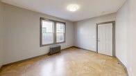 Located at 12-16 Groton St in Hartford, CT, this single-floor unit offers three bedrooms, one bathroom, and a hallway within a compact yet efficiently arranged floor plan. The bedrooms feature rich hardwood-style flooring and gray-framed windows that invite generous natural light and street-level views of the surrounding neighborhood. Cast-iron radiators in the bedrooms provide classic, reliable heating. The spacious primary bedroom is notably generous in size, offering ample room for furnishings and comfortable living. One bedroom features large-format tile flooring, adding variety to the unit's interior finishes. A hallway connects the rooms, contributing to a logical and functional layout. The bathroom is a standout feature, finished with elegant marble-look wall tiles accented by a decorative mosaic border in navy and black. A soaking tub with chrome fixtures and a frosted window for natural light complete the refined bathroom design. Neutral gray walls throughout the unit create a clean, versatile backdrop. The unit connects to a tiled entry area with a curved wall detail, adding a subtle architectural touch. Overall, the space offers a practical and well-appointed layout suited for everyday living in Hartford.