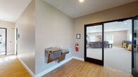 This single-floor community amenity building offers a well-rounded set of shared spaces designed to support an active and social lifestyle. The welcoming entryway features warm wood-look flooring, a wall-mounted dual drinking fountain, and glass-panel doors that open into the main gathering areas.

The lounge area provides a comfortable retreat, with plush upholstered sofas, a corner fireplace with a classic white mantel, a wall-mounted television, and multiple windows that invite natural light. The neutral, warm-toned walls and carpet throughout create a cohesive and relaxed ambiance.

Adjacent to the lounge is a spacious multipurpose room, currently configured with stackable seating and decorative artwork, offering flexibility for events and gatherings. A well-appointed kitchenette supports these functions with rich cherry wood cabinetry, light granite countertops, a sink, and a microwave.

The fitness center spans a generously sized area across two connected rooms, equipped with cardio machines including ellipticals, stationary bikes, and a treadmill. Large windows provide ample natural light, and a full-length wall mirror enhances the open feel. Recessed lighting, exit signage, and fire safety equipment are present throughout.

ADA-accessible restrooms complete the facility, finished with stone-look tile on both the floors and walls, and outfitted with grab bars for safety and accessibility.