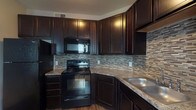 Located at 6667 Wesbury Park Ave in Columbus, Ohio, this single-floor residence offers a well-designed layout with thoughtfully appointed interiors throughout. The kitchen serves as a standout feature, showcasing rich dark espresso cabinetry that extends to the ceiling, providing ample storage. Granite-style countertops, a mosaic tile backsplash, black appliances including a refrigerator, electric range, built-in microwave, and dishwasher, and wood-look flooring complete this functional and stylish space. A breakfast bar peninsula connects the kitchen to the open-concept living and dining area, which is finished with plush neutral carpeting, bold charcoal accent walls, and multiple windows that invite natural light. The spacious bedrooms continue the carpeted flooring and feature the same contrasting accent walls, with at least one room offering access to a generous walk-in closet. The bathroom is outfitted with dark wood-finish cabinetry, a white single-sink vanity, a framed mirror, and a full tub-shower combination, accented by wood-look tile flooring. A separate entry area with multiple closet doors adds practical storage. The cohesive color palette and consistent finishes give the space a modern, polished ambiance throughout.
