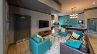 Located at 120 Plantation Creek Dr in Mooresville, NC, this single-floor community clubhouse delivers a well-appointed gathering space designed for both relaxation and productivity. The open layout flows seamlessly across multiple functional zones, all unified by warm hardwood-style flooring, bold teal accent walls, and rich brown trim that together create a cohesive, contemporary aesthetic.

The central game and lounge area serves as the heart of the space, anchored by a full-size pool table beneath a striking multi-bulb chandelier. Teal upholstered seating, patterned area rugs, and a wall-mounted flat-screen TV furnish the lounge zone, encouraging casual gathering. A dining-height table with dark chairs provides additional seating for group use.

A standout architectural feature is a floor-to-ceiling stacked stone column that anchors the business center area, where workstations with desktop computers are arranged for resident use. Pendant lighting illuminates the workspace, which is framed by a textured accent wall adding depth and visual interest.

A cozy nook with a round bistro table, leather chairs, decorative mirrors, and woven wall art creates an intimate setting for smaller conversations. Throughout, recessed lighting and carefully chosen décor contribute to a polished, inviting ambiance.
