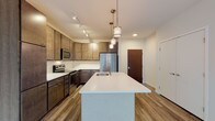 This single-floor residence showcases a thoughtfully designed open layout, with the kitchen serving as a clear centerpiece. The kitchen is outfitted with rich, dark wood cabinetry extending to the ceiling, offering generous storage capacity. White quartz countertops provide a crisp contrast, while a classic subway tile backsplash adds texture to the space. A substantial kitchen island with an undermount sink and pendant lighting above anchors the room, creating both a functional workspace and a natural gathering point. Stainless steel appliances, including a refrigerator, range, and microwave, complete the culinary setup. Wood-look plank flooring runs throughout the kitchen and living areas, adding warmth and continuity.

The bedrooms are finished with neutral-toned carpet, contributing to a quiet and comfortable atmosphere. Large black-framed windows allow natural light to fill these rooms while providing views of the surrounding exterior. A ceiling fan in one bedroom enhances comfort year-round.

The bathroom features light large-format tile flooring, a sliding glass shower enclosure, and a dark wood vanity with a white countertop, maintaining the same modern aesthetic found throughout the residence. Overall, the space presents a clean, contemporary design with consistent finishes.