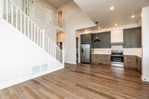 This two-story home showcases a contemporary design with a thoughtful blend of modern finishes and functional layout. The main floor centers around an open-concept living area with warm hardwood flooring, soaring ceilings, and a white-balustrade staircase that rises to an open upper landing, creating a striking sense of vertical space. Natural light flows freely through multiple windows, enhancing the bright, airy atmosphere.

The kitchen is well-appointed with two-tone cabinetry — sage-green upper cabinets paired with wood-grain lower cabinets — complemented by white quartz countertops, a subway tile backsplash, stainless steel appliances including a French door refrigerator and electric range, and a statement pendant light. A secondary entry door with glass paneling provides convenient access alongside the kitchen sink area.

Upper-level bedrooms feature plush carpeting and generous closet space, including a walk-in closet and sliding-door closets. The bathrooms are elegantly finished with large-format marble-look tile. One bathroom includes a frameless glass sliding shower with matte black hardware and built-in shelving, while another features a soaking tub surrounded by floor-to-ceiling marble-style tile, both conveying a refined, spa-like quality throughout.