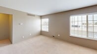 Located at 2191 E 14 Mile Rd in Sterling Heights, Michigan, this one-bedroom, one-bathroom unit offers a well-organized single-floor layout that makes efficient use of its space. The entrance leads into a combined kitchen and living area, where rich warm-toned wood cabinetry pairs with dark granite-style countertops and black appliances, including a gas range, refrigerator, and built-in microwave. Wood-look flooring runs throughout the kitchen, while a ceiling fan overhead adds comfort to the open living zone. The spacious bedroom is finished with soft wall-to-wall carpeting, neutral taupe walls, and multiple windows fitted with blinds that allow for ample natural light. A ceiling fan with light fixture adds functionality, and the room connects conveniently to a dedicated closet and the full bathroom. The bathroom features a full-size soaking tub with a tiled surround and a curved shower curtain rod. A hallway connects the main living areas to the private quarters, providing a clear separation between the living and sleeping spaces. Overall, the unit presents a clean, neutral palette throughout, offering a practical and comfortable living environment.