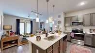 This single-story, 3-bedroom, 1-bathroom residence delivers a functional and stylish layout across a compact yet efficient floor plan. The open-concept kitchen serves as the centerpiece of the living area, featuring a large quartz-topped island with an undermount sink and pendant lighting overhead. Taupe-toned cabinetry, a subway tile backsplash, and stainless steel appliances — including a refrigerator, range, microwave, and dishwasher — complete the kitchen. Wood-look flooring flows seamlessly into the living room, which is brightened by sliding glass doors that invite natural light and provide outdoor access. A ceiling fan adds comfort to the space. The primary bedroom is generously sized, offering carpet flooring, large windows, an outdoor access door, and a ceiling fan. It is accompanied by a dedicated walk-in closet with multi-tiered shelving and hanging rods. Two additional bedrooms share similar finishes and closet storage. The shared bathroom features a dual-sink vanity with a quartz countertop, gray cabinetry, a wide mirror with lighted fixtures, and a tiled walk-in shower. A hallway connects all rooms, and two closets provide added storage throughout the residence.