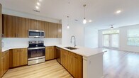 This single-floor unit showcases a contemporary design centered around an open-concept layout that seamlessly connects the kitchen and living area. The kitchen is a standout feature, equipped with stainless steel appliances including a French door refrigerator, range, microwave, and dishwasher. Warm wood-grain cabinetry extends from floor to ceiling, providing generous storage, while a large peninsula island with a white quartz countertop and undermount sink serves as both a functional workspace and a natural divider between the kitchen and living area. Pendant lighting above the island adds a refined touch, and light wood-style flooring runs throughout the main living space, enhancing the airy feel. The bedrooms feature plush carpeting and receive natural light through sizable windows. A walk-in closet with multi-tier wire shelving offers substantial storage capacity. Two bathrooms are finished with large-format tile flooring and dark wood vanities with white countertops. One bathroom includes a tub-shower combination, while the other features a glass-enclosed shower stall. Clean white walls and recessed lighting throughout contribute to the overall bright, modern ambiance of this well-appointed space.
