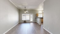 Located at 4905 Castana Ave in Lakewood, CA, this single-floor unit offers a thoughtfully arranged layout comprising a living room, kitchen, bathroom, and hallway. The living room is bright and open, featuring crown molding, a ceiling fan with light fixture, and wood-look flooring that extends throughout the space. Natural light filters in through a large window with blinds, accompanied by a glass door that provides outdoor access. A wall-mounted HVAC unit ensures year-round comfort. The kitchen is defined by a peninsula counter with dark granite-style countertops, light wood cabinetry, a stainless steel sink, and a pendant light overhead — all positioned to connect seamlessly with the living area for an open-concept feel. A short staircase with a handrail in the hallway area leads to the unit's entrance, reinforcing the split-level entry characteristic. The bathroom is clean and functional, outfitted with a full soaking tub and shower combination, a toilet, wood-look flooring, and a frosted window above the tub for natural ventilation and light. Soft gray walls and white trim are consistent throughout, creating a cohesive, neutral aesthetic that lends itself well to a variety of interior styles.