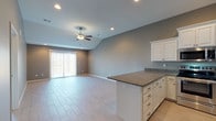 This single-story home showcases a thoughtfully designed open-concept layout that seamlessly connects the kitchen and living area. The living space features striking vaulted ceilings accented by a ceiling fan, recessed lighting, and light-toned tile flooring, creating an airy and expansive atmosphere. A sliding glass door allows natural light to flow in and provides outdoor access.

The kitchen is well-appointed with white cabinetry, granite countertops, stainless steel appliances including a refrigerator, range, and microwave, and a peninsula that serves as both a workspace and casual dining area. Recessed lighting illuminates the space effectively throughout.

The primary bedroom stands out with an elegant tray ceiling, ceiling fan, plush carpeting, and a walk-in closet. Additional bedrooms are carpeted and receive natural light through blinded windows, offering comfortable and functional spaces. Each room is painted in a consistent warm gray palette that ties the home together cohesively.

The bathroom features a granite-topped vanity with an undermount sink, a walk-in shower with glass sliding doors, and a window providing natural light. Throughout the home, neutral tones, consistent finishes, and practical design elements contribute to a clean, modern aesthetic.