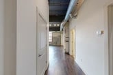 Located at 220 Herald Pl in Syracuse, NY, this industrial-style loft blends historic character with modern finishes across a single, well-appointed floor. The open living area immediately impresses with its soaring dark-painted ceilings, exposed silver ductwork, and rich hardwood flooring that runs throughout the main living spaces. Original brick walls add raw, authentic texture, while oversized factory-style windows framed in deep red bathe the interior in abundant natural light and offer views of the surrounding cityscape.

The kitchen is a standout, featuring rich mahogany cabinetry, granite countertops, stainless steel appliances, and a breakfast bar with pendant lighting — ideal for both everyday living and entertaining. The spacious primary bedroom continues the industrial aesthetic with exposed brick accents, large multi-pane windows, and plush carpeting for comfort.

Two full bathrooms provide practical functionality: one offers a walk-in glass-enclosed shower with tile surround and dark vanity cabinetry, while the second features tile flooring, a granite-topped vanity, and a glass-paneled shower. Additional spaces include a hallway, two closets, a utility room, and an unclassified flex room. This loft offers a compelling urban living experience rooted in architectural heritage.