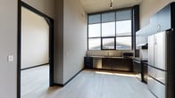 Located at 230 East Ave in Norwalk, Connecticut, this modern loft-style unit showcases an industrial-contemporary design with impressively tall ceilings that lend a dramatic sense of volume throughout the open living area. Light-toned hardwood flooring runs continuously across the main living spaces, complementing the neutral gray walls and bold dark trim for a refined, modern aesthetic.

The kitchen is outfitted with dark cabinetry, stainless steel appliances including a refrigerator, range with hood, dishwasher, and microwave, paired with a classic white tile backsplash. Floor-to-ceiling industrial-style windows flood the kitchen and adjacent living area with abundant natural light while offering views of the surrounding neighborhood.

The bedroom benefits from its own set of large windows, continuing the theme of natural light and open atmosphere. A spacious walk-in closet fitted with wire shelving systems provides generous storage capacity. The bathroom features dark cabinetry with a wide vanity, stainless steel countertop, a large mirror, tiled shower, and wood-look tile flooring, creating a clean and functional space. Track lighting throughout adds a modern, versatile touch. This unit offers a compelling blend of urban industrial character and contemporary finishes.
