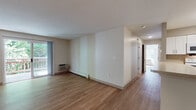 Located at 100 Tower St in Hudson, Massachusetts, this single-floor unit offers a clean, functional layout with a bright and open feel throughout. Warm hardwood-style flooring runs continuously across the living areas and bedrooms, lending a cohesive and inviting aesthetic to the entire space.

The spacious living area is bathed in natural light, with sliding glass doors opening directly onto a private balcony that overlooks lush, mature greenery — an ideal setting for relaxing or enjoying the outdoors. Baseboard heating and wall-mounted air conditioning units are present throughout, ensuring year-round comfort.

The kitchen features white shaker-style cabinetry with ample storage, light countertops, and a full suite of white appliances including a refrigerator, electric range, built-in microwave, and dishwasher. A peninsula counter connects the kitchen to the open living and dining area, making the space well-suited for both everyday living and entertaining.

The bedrooms are generously sized, each benefiting from multiple windows that frame wooded outdoor views and fill the rooms with natural light. Two bathrooms serve the unit — one equipped with a combined shower and tub, the other with a standalone shower stall — both finished with tile flooring and white vanity cabinetry.