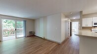 Located at 100 Tower St in Hudson, Massachusetts, this single-floor unit offers a clean, functional layout with a bright and open feel throughout. Warm hardwood-style flooring runs continuously across the living areas and bedrooms, lending a cohesive and inviting aesthetic to the entire space.

The spacious living area is bathed in natural light, with sliding glass doors opening directly onto a private balcony that overlooks lush, mature greenery — an ideal setting for relaxing or enjoying the outdoors. Baseboard heating and wall-mounted air conditioning units are present throughout, ensuring year-round comfort.

The kitchen features white shaker-style cabinetry with ample storage, light countertops, and a full suite of white appliances including a refrigerator, electric range, built-in microwave, and dishwasher. A peninsula counter connects the kitchen to the open living and dining area, making the space well-suited for both everyday living and entertaining.

The bedrooms are generously sized, each benefiting from multiple windows that frame wooded outdoor views and fill the rooms with natural light. Two bathrooms serve the unit — one equipped with a combined shower and tub, the other with a standalone shower stall — both finished with tile flooring and white vanity cabinetry.