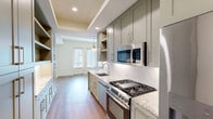 Located at 10520 Lakeline Mall Dr in Austin, TX, this efficiently designed single-floor unit offers a well-appointed layout comprising a kitchen, living room, bathroom, closet, and entrance. The galley-style kitchen is a standout feature, showcasing sage-green cabinetry with open shelving, granite countertops, a white subway tile backsplash, stainless steel appliances including a gas range, built-in microwave, and dishwasher, and a tray ceiling with recessed lighting that adds architectural depth. A pendant light anchors the kitchen's transition into the living area, which features warm hardwood-style flooring throughout. The living room is bright and airy, bathed in natural light through a set of large windows flanking a glass-paneled door that opens to a balcony, creating a seamless indoor-outdoor connection. The bathroom is elegantly finished with large-format marble-look tile flooring, a dark-toned vanity topped with granite, a framed mirror, and a full tub-shower combination with white subway tile surround. Clean lines, neutral tones, and quality finishes are consistent throughout, giving the space a cohesive, modern aesthetic that maximizes both comfort and functionality.