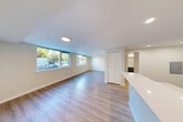 Located at 1221 NE 180th St in Shoreline, WA, this efficiently designed single-floor studio offers a clean, contemporary layout that makes smart use of its space. Light-toned luxury vinyl plank flooring runs throughout, lending a cohesive, modern aesthetic to every area.

The open-concept kitchen and living room serve as the heart of the unit. The kitchen is well-appointed with dark, textured cabinetry extending to the ceiling, crisp white quartz countertops, a suite of black appliances including a refrigerator, range, and over-the-range microwave, and a peninsula with an undermount sink that doubles as a breakfast bar and natural divider between the kitchen and living area. Recessed and linear overhead lighting keeps the space bright and functional.

The living area is open and airy, benefiting from multiple large windows that invite generous natural light and offer views of the surrounding neighborhood's greenery. A slatted double closet door provides convenient built-in storage.

The bathroom is clean and simply finished, featuring light vinyl flooring consistent with the rest of the unit, a full tub-shower combination with a curved curtain rod, a vanity, and recessed ceiling lighting. A utility closet with a wire shelving rack adds additional storage near the entry.