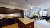 Located at 921 S Orlando Ave in Maitland, Florida, this single-floor residence offers a thoughtfully designed layout that balances functionality with style. The heart of the home is a well-equipped gourmet kitchen featuring rich dark wood cabinetry, granite countertops, a large central island with pendant lighting, and stainless steel appliances including a refrigerator and built-in microwave. Warm hardwood flooring flows throughout the kitchen, complemented by track lighting overhead. The kitchen opens seamlessly into a dedicated dining area, where crown molding and a trio of decorative wall mirrors add elegance and depth to the space. The living room is bright and welcoming, with natural light filtering through large windows dressed in sheer curtains, plush carpeting underfoot, and a ceiling fan adding comfort. The bedroom is a cozy retreat, highlighted by carpeted floors, ample natural light from well-framed windows, and a ceiling fan. The bathroom is finished with matching dark wood cabinetry, granite countertops, a wide vanity mirror, and hardwood-style flooring, maintaining a consistent design language throughout. Crown molding, coordinated finishes, and an open, flowing floor plan give this residence a polished and cohesive character.