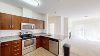 This thoughtfully designed one-bedroom, one-bathroom residence offers an efficient and comfortable layout across a single floor. The open-concept kitchen and living area serves as the heart of the home, where rich dark-wood cabinetry, granite countertops, and a full suite of stainless steel appliances — including a refrigerator, electric range, microwave, and dishwasher — come together to create a functional and stylish kitchen. Wood-look flooring runs throughout the kitchen, while a peninsula counter provides a natural transition into the living room. The living room is highlighted by a classic fireplace set against a clean white surround, adding warmth and character to the space. Natural light filters in through sliding glass doors, enhancing the bright and airy feel of the room, which features soft, neutral-toned carpeting. The bedroom offers a comfortable and quiet retreat, carpeted for comfort, with a window fitted with blinds allowing for controlled natural light. A closet provides dedicated storage space. The bathroom is clean and efficiently designed, featuring a tub-shower combination with tile surround, a granite-topped vanity with dark wood cabinetry, and a mirrored medicine cabinet.