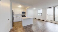 This thoughtfully laid-out 1-bedroom, 1-bathroom unit offers a practical and modern living experience across a single floor. The open-concept kitchen and living room serve as the heart of the space, featuring light hardwood-style flooring that runs throughout, crisp white walls, and an abundance of natural light streaming in through large sliding glass doors that lead to a private balcony with outdoor views of the surrounding neighborhood.

The kitchen is well-appointed with white cabinetry, granite-look countertops, a central peninsula ideal for casual dining or food preparation, and a full suite of stainless steel appliances including a range, over-the-range microwave, and refrigerator. A subway tile backsplash and undermount sink add clean, contemporary touches.

The living area is bright and open, benefiting from floor-to-ceiling sliding doors and additional windows that invite natural light while providing easy access to the balcony. Baseboard heating runs along the exterior walls throughout the unit.

The bedroom is a comfortable, private retreat with a window overlooking the outdoors and ample wall space. The full bathroom features large-format wall tile in a warm taupe tone surrounding a soaking tub and shower combination, complemented by light tile flooring for a clean, classic finish.