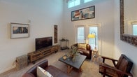 This single-floor residence is thoughtfully designed to maximize both comfort and functionality. The living room serves as a focal point of the home, boasting dramatically high ceilings with clerestory windows that draw in abundant natural light. French doors lead to an outdoor area, enhancing the sense of openness, while plush carpeting and ample wall space create a warm, welcoming atmosphere.

The kitchen is outfitted with white shaker-style cabinetry, granite countertops, a subway tile backsplash, and white appliances including a range, microwave, and refrigerator. Light wood-look flooring and track lighting complete the clean, contemporary aesthetic.

The primary bedroom features a tray ceiling, soft carpet, and a large window, with direct access to a spacious en-suite bathroom. This bathroom includes a granite-topped vanity with white cabinetry, wood-look tile flooring, and a shower. A second bedroom and an additional full bathroom with similar finishes provide flexible accommodations.

A dedicated laundry area houses a full-size top-load washer and dryer alongside a tall storage cabinet, adding practical convenience. Throughout the residence, a cohesive neutral palette and consistent finishes create a unified, polished living environment.