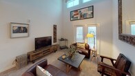 This single-floor residence is thoughtfully designed to maximize both comfort and functionality. The living room serves as a focal point of the home, boasting dramatically high ceilings with clerestory windows that draw in abundant natural light. French doors lead to an outdoor area, enhancing the sense of openness, while plush carpeting and ample wall space create a warm, welcoming atmosphere.

The kitchen is outfitted with white shaker-style cabinetry, granite countertops, a subway tile backsplash, and white appliances including a range, microwave, and refrigerator. Light wood-look flooring and track lighting complete the clean, contemporary aesthetic.

The primary bedroom features a tray ceiling, soft carpet, and a large window, with direct access to a spacious en-suite bathroom. This bathroom includes a granite-topped vanity with white cabinetry, wood-look tile flooring, and a shower. A second bedroom and an additional full bathroom with similar finishes provide flexible accommodations.

A dedicated laundry area houses a full-size top-load washer and dryer alongside a tall storage cabinet, adding practical convenience. Throughout the residence, a cohesive neutral palette and consistent finishes create a unified, polished living environment.