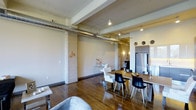 Located in Dallas, this urban loft showcases a compelling blend of industrial character and contemporary design. The open-concept layout flows seamlessly from the living area through to the dining and kitchen spaces, creating a sense of expansive, connected living. Rich hardwood floors run throughout, grounding the space with warmth and texture.

Architectural details are a defining feature here. Exposed concrete columns, visible overhead ductwork, and structural ceiling beams lend a raw, industrial aesthetic that is balanced by modern finishes and thoughtful furnishings. The elevated ceilings amplify the sense of openness and volume throughout the space.

The dining area is anchored by a substantial wood table surrounded by a mix of modern black and white chairs, creating a striking visual contrast. Nearby, the kitchen features sleek cabinetry and stainless steel appliances, including a full-sized refrigerator, offering a clean and functional counterpoint to the industrial surroundings. Track lighting and accent fixtures provide layered illumination throughout, complementing the open layout.

The living area is partially visible and hints at a comfortable, curated setup. Overall, the space delivers a sophisticated urban atmosphere with an engaging mix of raw architectural elements and modern design sensibilities.