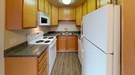 This 2-bedroom, 1-bathroom unit is thoughtfully laid out across a single floor, offering a comfortable and functional living environment. The living room features wood-look vinyl plank flooring, crown molding, a ceiling fan, and a large floor-to-ceiling vertical blind window treatment that allows an abundance of natural light to fill the space. The open flow leads directly into a well-equipped kitchen outfitted with warm wood cabinetry, dark granite-style countertops, and white appliances including a refrigerator, electric range, built-in microwave, and double-basin sink. Both bedrooms are carpeted and generously sized, each featuring large windows with vertical blinds and baseboard heating. The primary bedroom includes convenient access to a closet as well as direct entry to the bathroom. The full bathroom is clean and functional, featuring a single-sink vanity with a stone-tone countertop, a medicine cabinet mirror, and a shower-tub combination. Wood-look flooring extends throughout the bathroom, complementing the neutral, light-toned walls found throughout the unit. The overall design is clean and understated, providing a versatile canvas suitable for a variety of living styles.