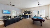 Located at 9511 NE Hazel Dell Ave in Vancouver, Washington, this single-story community clubhouse is designed to offer a well-rounded gathering space with a variety of functional amenities. The facility is defined by its soaring vaulted ceilings and an abundance of natural light streaming through large windows, creating an open and welcoming atmosphere throughout.

The main lounge area features comfortable seating arrangements, including plush leather sofas and accent chairs, centered around a wall-mounted flat-screen television. A dedicated game area includes a full-size billiards table, while a separate seating nook provides a quieter spot with armchairs and a chess table for more intimate gatherings.

The fully equipped kitchen is appointed with dark cabinetry, granite countertops with under-cabinet lighting, stainless steel appliances including a refrigerator and microwave, and bar-height seating along the counter — ideal for casual dining or entertaining.

A business center area offers multiple computer workstations beneath tall, light-filled windows, providing a practical workspace within the community. The entryway features double-height ceilings, a drinking fountain, and access to restrooms, lending the space a civic, professional character. Tile flooring in the kitchen transitions to neutral carpet tile throughout the main areas, grounding the contemporary design with warmth and functionality.