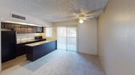 Located along East Camelback Road in Scottsdale, Arizona, this single-story unit offers a practical and functional layout suited to everyday living. The open-concept living and kitchen area forms the heart of the space, where plush carpeting covers the living area floor while wood-style flooring runs through the kitchen. A ceiling fan provides overhead circulation, and a sliding glass door lined with vertical blinds opens to an outdoor area, allowing natural light to filter into the living space.

The kitchen is equipped with dark espresso cabinetry offering generous upper and lower storage, granite-style countertops, and a matching peninsula that serves as a natural divider between the kitchen and living areas. Black appliances, including a refrigerator, electric range, and dishwasher, are integrated throughout, along with a double basin sink positioned beneath a window.

The bedroom features soft carpeting, a textured ceiling, a ceiling fan, and a window with blinds that provides natural light and outdoor views. A built-in closet with shelving and hanging space offers organized storage. The bathroom includes a tub and shower combination with chrome fixtures. Textured walls are consistent throughout the unit, contributing to its overall character.