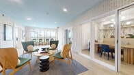 This single-floor amenity space is thoughtfully designed to serve as a multifunctional community hub. The interior is unified by a distinctive gold-and-cream patterned wallcovering that adds warmth and visual texture throughout, complemented by light wood-look flooring that extends seamlessly across all areas.

The central lounge area features a curated seating arrangement of sculptural green wingback chairs and natural wood accent chairs gathered around a rounded coffee table and stacked cylindrical side tables, all anchored by a blue-toned area rug. Recessed lighting and a soft blue-painted ceiling in portions of the space contribute to an airy, welcoming atmosphere.

Adjacent to the lounge, glass-paneled French doors open into a private conference or co-working room furnished with a wooden table and blue chairs, offering a dedicated space for focused work or meetings. A separate office or private room is accessible via a keypad-secured door along the patterned wall.

A mail and package alcove is positioned nearby, featuring a bank of individual mailboxes illuminated by warm sconce lighting. Large windows and a glazed door lead to an outdoor area with bar-height seating, providing views of the surrounding landscape and an extension of the social space.