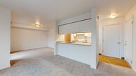 This efficiently designed 2-bedroom, 1-bathroom unit spans a single floor, offering a practical and well-organized layout. The open-concept kitchen and living area serves as the heart of the unit. The galley-style kitchen features white cabinetry with warm wood trim accents, laminate countertops, a stainless steel sink, and white appliances including an electric range and refrigerator. Light hardwood-style flooring runs throughout the kitchen, while a pass-through window connects the kitchen to the living area, enhancing the sense of openness. The living room is bright and airy, with large windows that allow natural light to fill the carpeted space and offer views of the surrounding neighborhood. A hallway connects the main living areas to the two bedrooms and full bathroom. The primary bedroom is generously sized with soft carpeting, a closet, and a window for natural light. The second bedroom is similarly appointed with carpet and a window. The full bathroom is clean and functional, featuring a combined tub and shower, a toilet, and a vanity with a single sink, warm countertop, and a large mirror. A hallway provides access to the unit's entrance, completing the straightforward and livable floor plan.