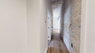 Located at 15 New St in West Hartford, CT, this single-floor space offers a thoughtfully designed layout that combines industrial character with contemporary finishes. Exposed brick walls and hardwood-style flooring run throughout, creating a warm yet modern aesthetic that carries seamlessly from room to room.

The hallway sets the tone immediately, showcasing a striking whitewashed brick accent wall alongside crisp white walls and track lighting overhead — a nod to the building's architectural heritage. The spacious kitchen is a functional highlight, featuring rich honey-toned cabinetry, dark granite countertops, and a full suite of stainless steel appliances including a refrigerator with ice maker, gas range, over-the-range microwave, and dishwasher. A kitchen island provides additional prep and counter space, while soaring ceilings lend an open, airy feel.

The living area benefits from multiple windows that invite natural light and offer views of the surrounding neighborhood. Bedrooms are generously sized with large windows and clean white walls, providing a bright and restful environment. The bathrooms are finished with classic white subway tile, bold black accent tile borders, and charming penny mosaic tile flooring — one bathroom features a dark granite vanity countertop for an elevated touch. Throughout, the space balances timeless design details with practical, modern amenities.