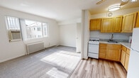 Located at 3710 Columbia Pike in Arlington, VA, this efficiently designed unit offers a well-organized single-floor layout comprising a combined living and dining area, a kitchen, a closet, and a full bathroom. The open living and dining space features neutral-toned carpet, bright white walls, and large windows that invite generous natural light while offering views of the surrounding neighborhood. A classic cast-iron radiator provides supplemental heating, complementing the room's functional design. The kitchen is positioned adjacent to the living area, partially separated by a half-wall partition. It is equipped with warm-toned wood cabinetry, granite-style countertops, a gas range, a full-size refrigerator, and a sink — all set atop easy-to-maintain wood-style flooring. A ceiling fan with integrated lighting adds airflow and illumination to the kitchen space. The bathroom is clean and straightforward, featuring a tiled tub-shower combination, a window for natural light and ventilation, a single vanity with sink, and a medicine cabinet mirror. The overall ambiance of the unit is bright, neutral, and practical, making efficient use of its compact footprint in a well-connected Arlington location.